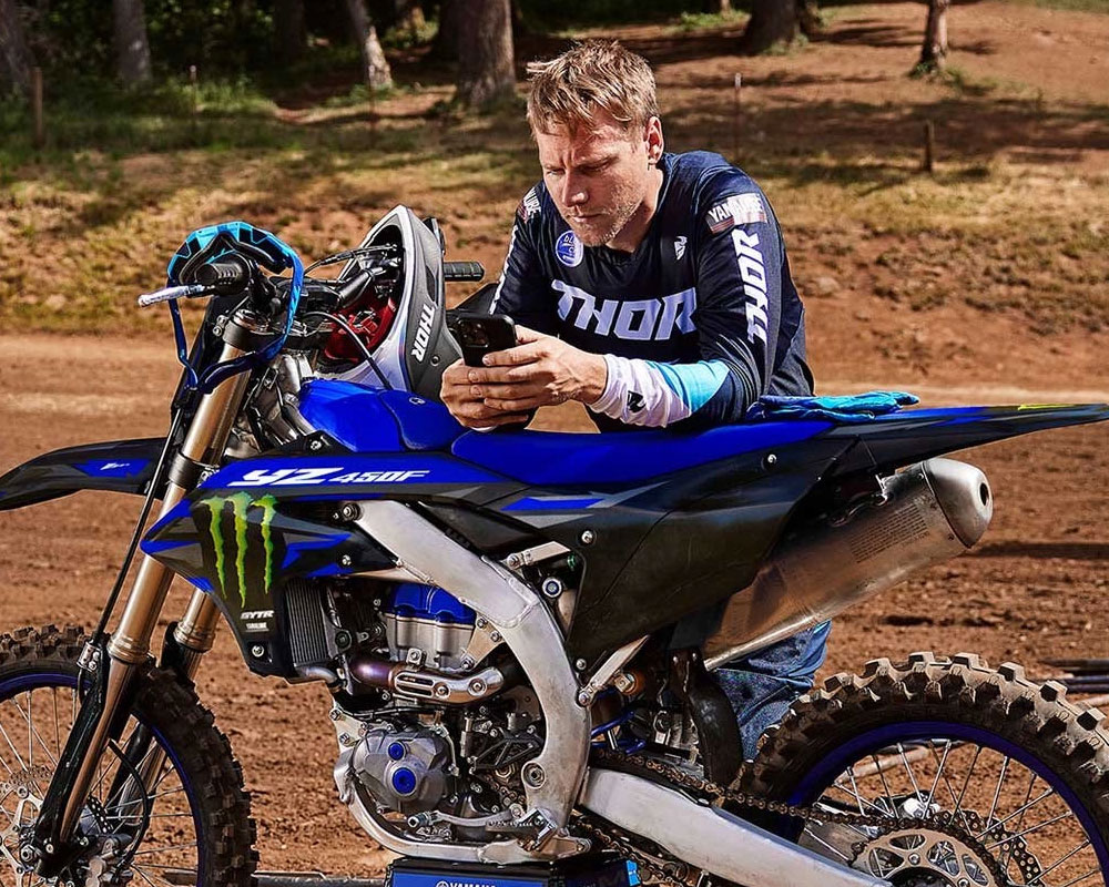 Power Tuner App shown on a phone with a rider leaned over a YZ450F using the app